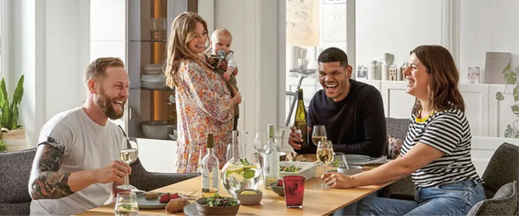 Helles Wohnzimmer mit zwei beigen Sofas, schwarzem Couchtisch, rotem Teppich und grüner Wand. Pflanzen, Regal und Stehleuchte schaffen ein modernes Wohnambiente mit gemütlicher Atmosphäre und natürlicher Raumgestaltung.